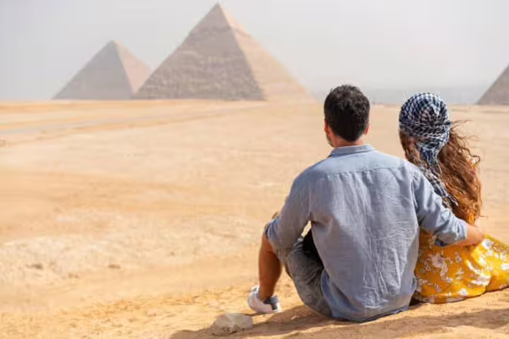Couple sitting in Giza desert facing pyramids, romantic Cairo photo session add-on tour with pro photos