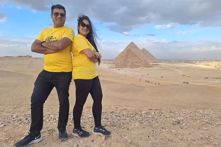 Couple in matching yellow shirts enjoying a scenic view of the Giza Pyramids on a private camel tour with lunch.