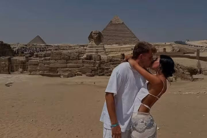 Couple embracing near the Great Sphinx and pyramids on VIP all-inclusive Giza tour with camel ride