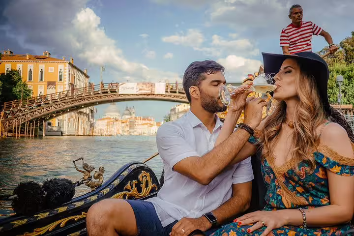 Couple enjoying an aperitif on a gondola ride under a Venetian bridge, soaking in the romantic ambiance.
