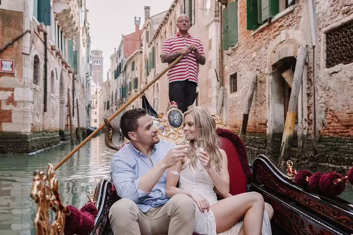 Couple toasting with champagne on a gondola in Venice, surrounded by historic canals and architecture.