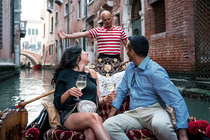 Couple enjoying a gondola ride with champagne, accompanied by a gondolier in Venice's charming canals.