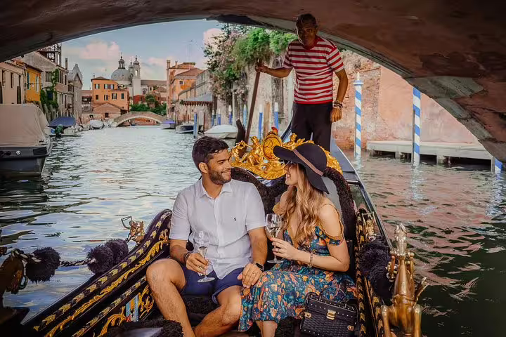 Couple savoring drinks on a gondola ride through Venice's picturesque canals, with a gondolier in traditional attire.