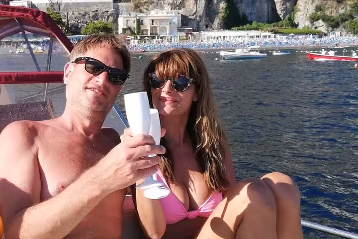 Smiling couple relaxing with drinks on a Classic Gozzo boat, taking in the scenic views of the Amalfi coast.