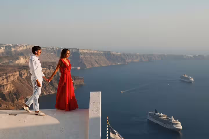 Couple holding hands on Santorini caldera cliff at sunset, captured by a proposal photographer with sea views