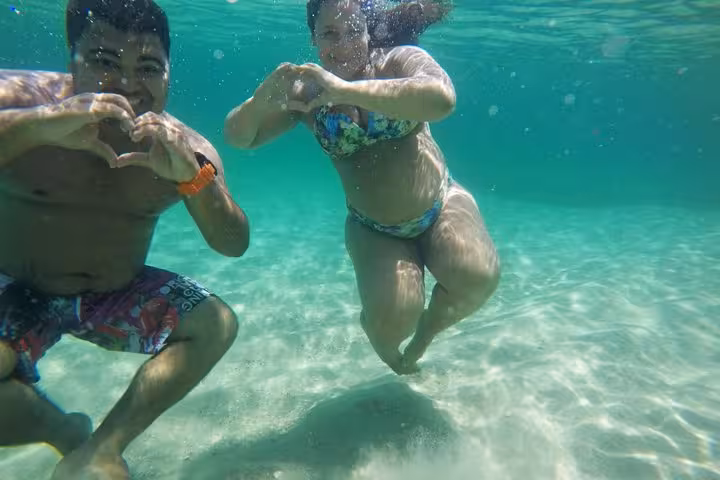 Couple making heart shapes underwater in the clear, turquoise waters of Lagoa Azul during a speedboat tour.
