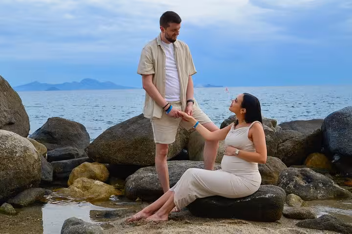 Couple holding hands on rocky Ammoudara beach, capturing a serene private photoshoot moment by the sea.