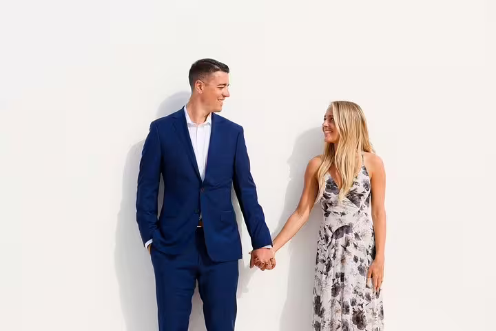 Stylish couple holding hands against a white wall in Santorini, ideal for a professional photographer tour.