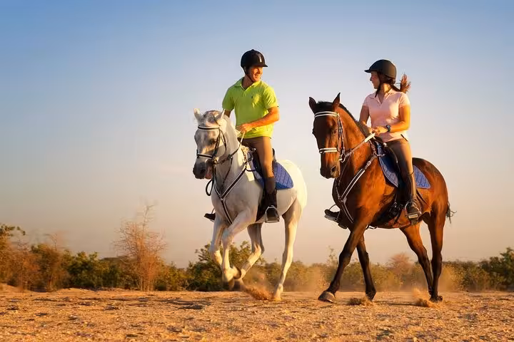 Couple riding horses in Hurghada desert at sunset, 2-hour horseback tour with helmeted riders