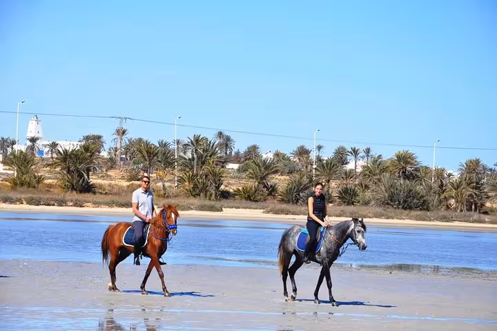 Couple riding horses on Marsa Alam beach at low tide, scenic Red Sea shoreline on 3-hour sunrise riding tour