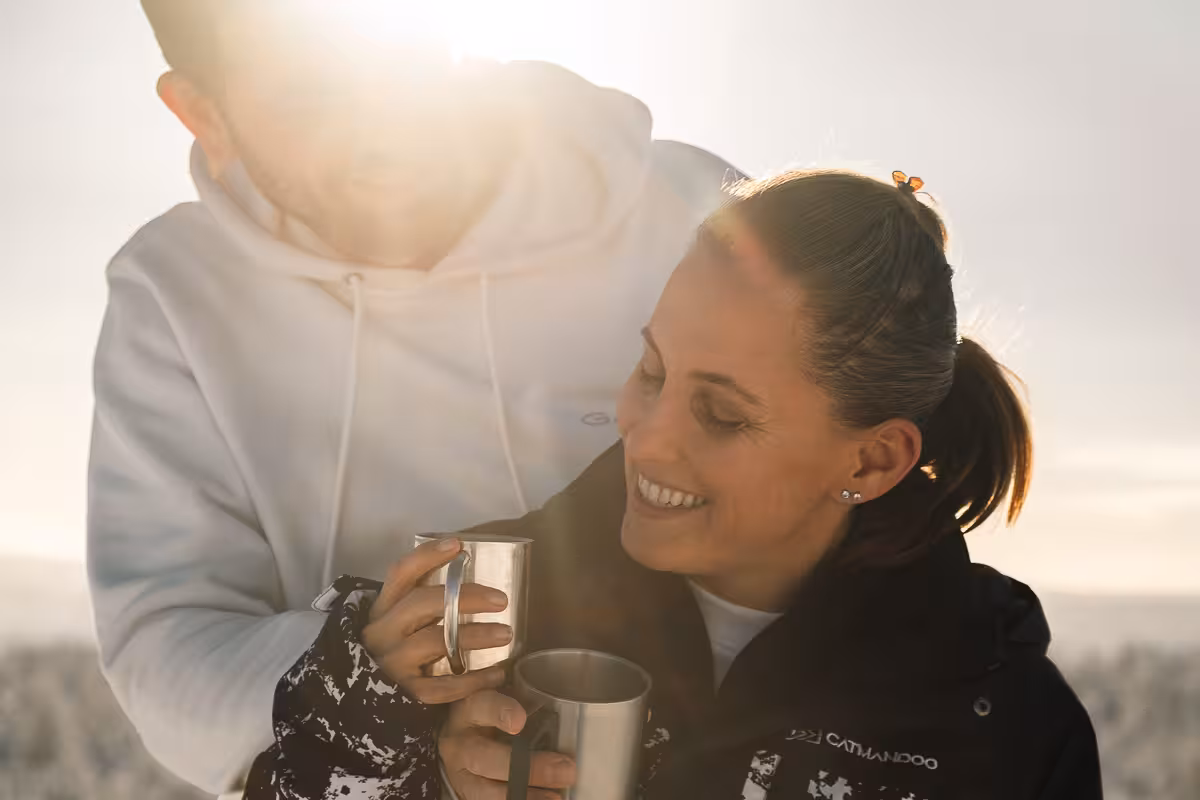 Couple enjoying hot drinks in winter sunlight during a private holiday photo session in Rovaniemi, Finland.