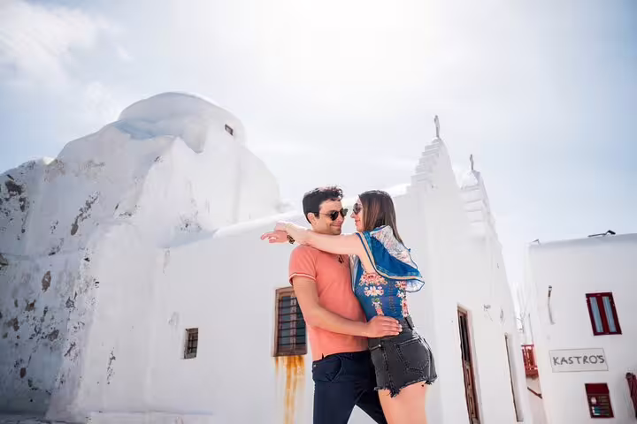 Couple hugging by white church in Mykonos for private photoshoot with professional photographer in Little Venice