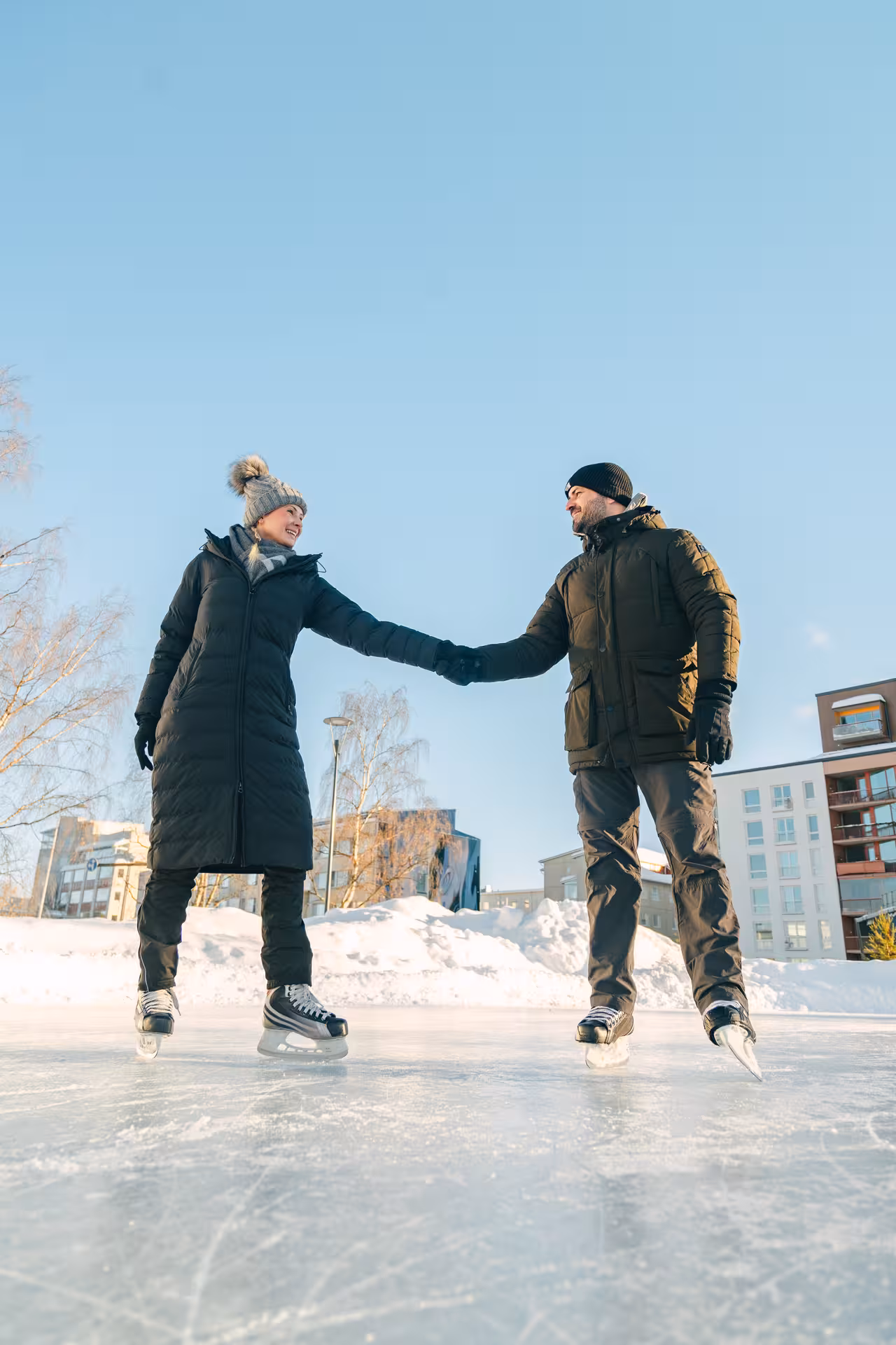 Smiling couple holding hands during an ice skating photography session in snowy Rovaniemi, Finland.