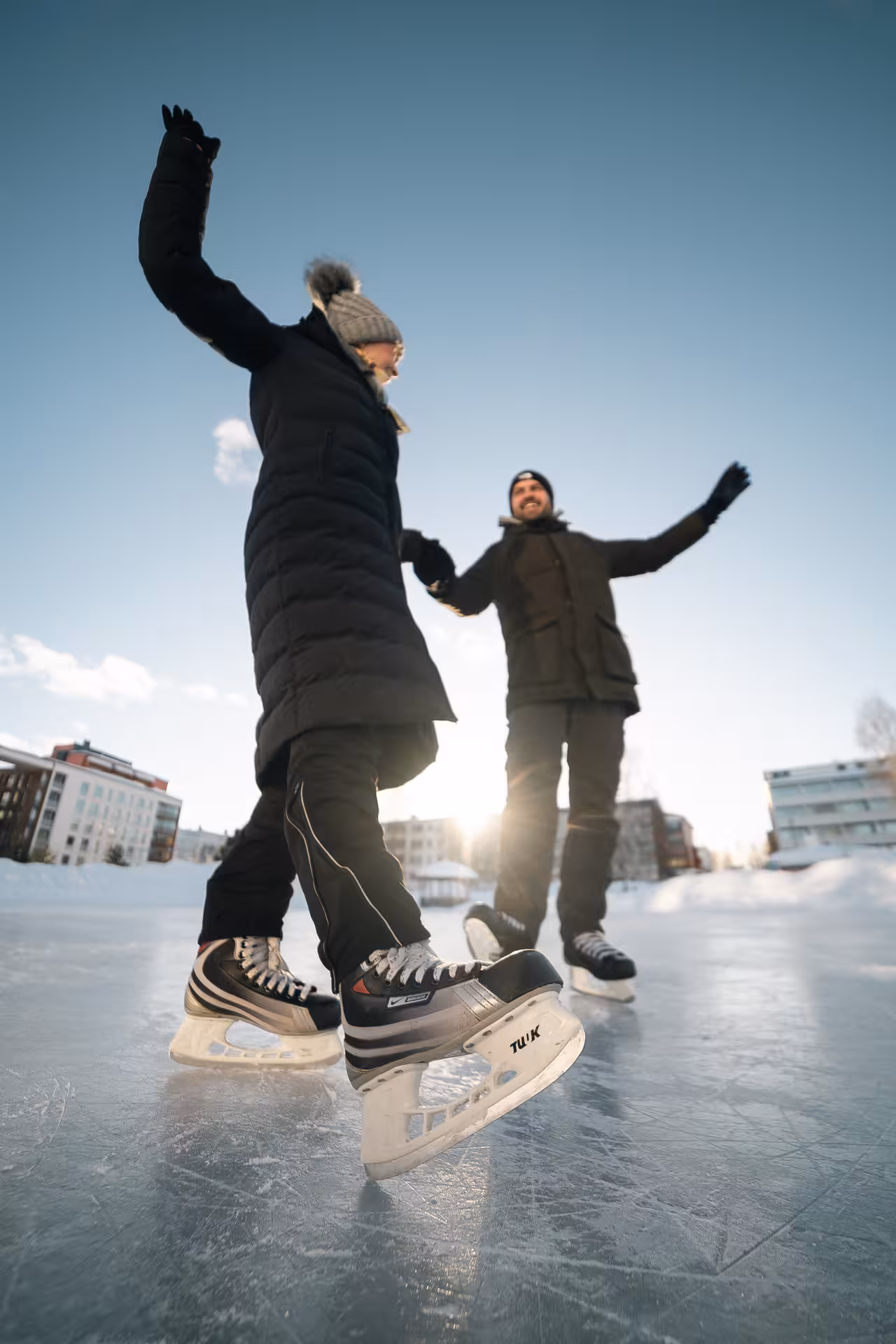Couple enjoying a private ice skating session in Rovaniemi under a clear blue sky, capturing joyful moments.