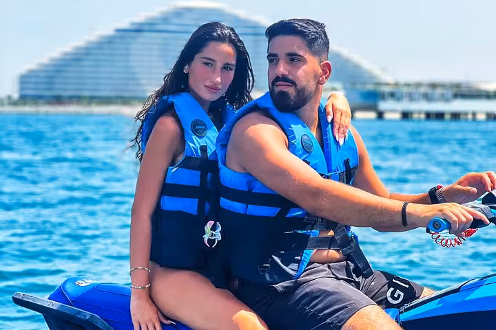 Close-up of a couple on a jet ski in Dubai, wearing life vests with a modern hotel in the background.
