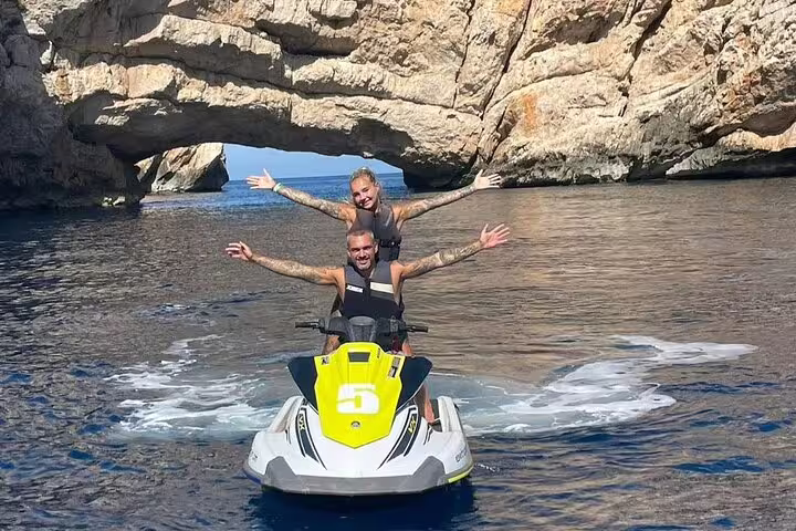 Couple on jet ski under rocky sea arch on Ibiza tour from San Antonio to Margaritas Islands
