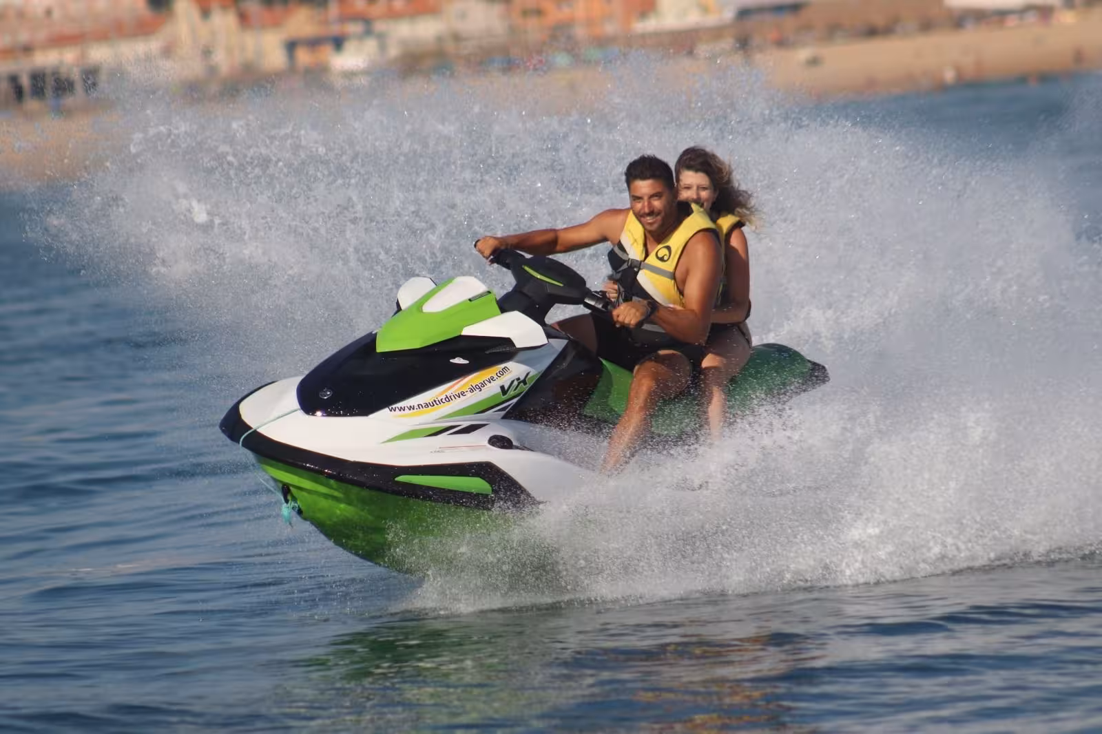Couple riding a fast jet ski at Praia dos Tomates Algarve, splashing through clear Atlantic waves on a sunny Portugal day