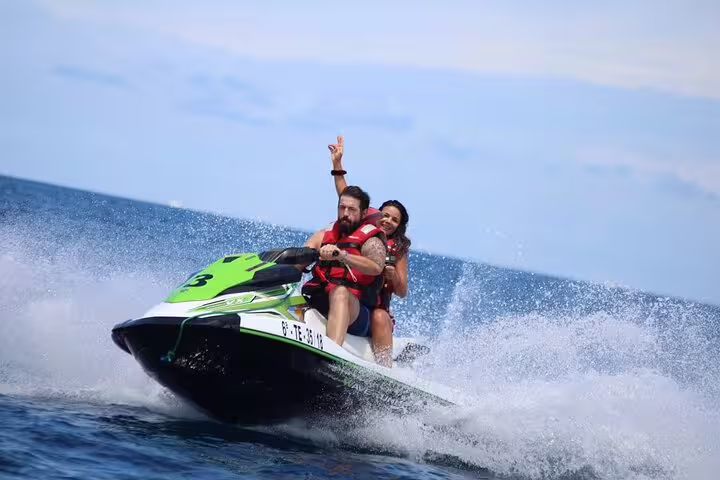 Couple experiencing an exhilarating jet ski safari with ocean spray under a clear blue sky.
