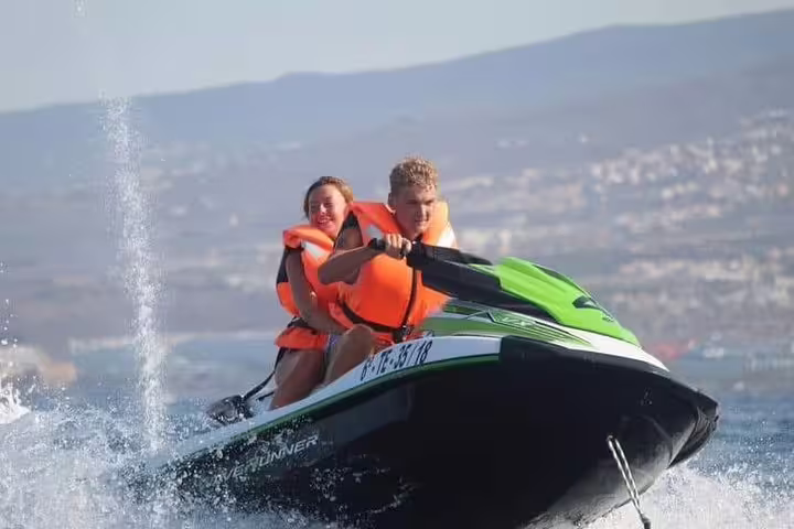 Excited pair navigating through waves on a jet ski, wearing life vests, on a lively 1-hour ocean safari experience.