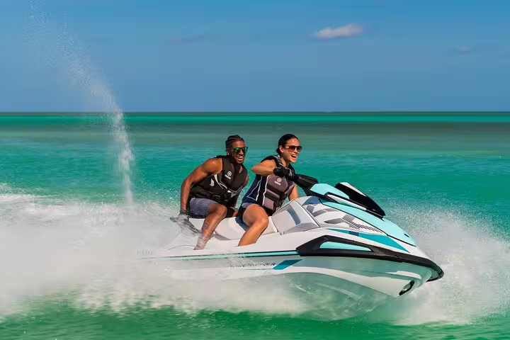 Couple riding jet ski tour from San Antonio Ibiza to Atlantis, carving through clear water with spray