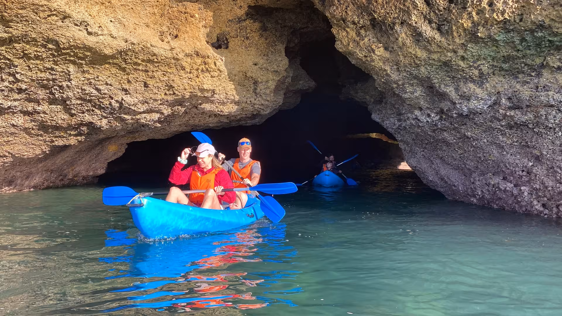 Couple kayaking through narrow Benagil cave passage at sunrise, discovering secluded Algarve grottoes and crystal-clear water