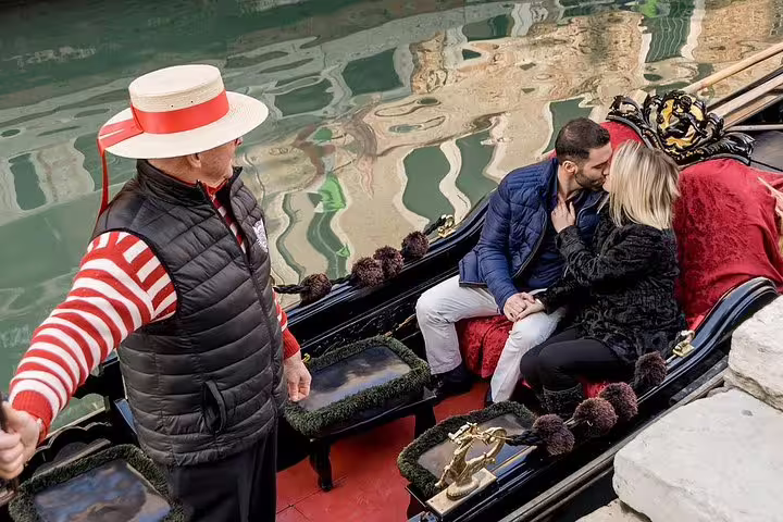 Couple shares a tender kiss on a gondola ride in Venice, accompanied by a traditional gondolier on a peaceful canal.