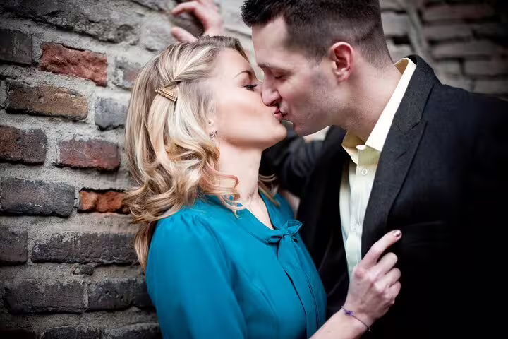 Couple shares a kiss against a rustic Verona brick wall, ideal for capturing intimate moments in a photoshoot.