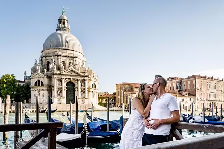 Couple sharing a kiss on a Venetian bridge with gondolas and historic architecture in the background.