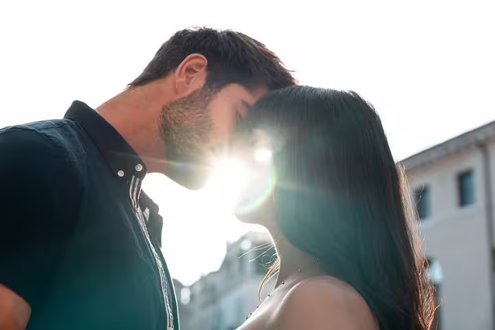 A couple kisses passionately under a bright sun flare in a picturesque Venetian setting.