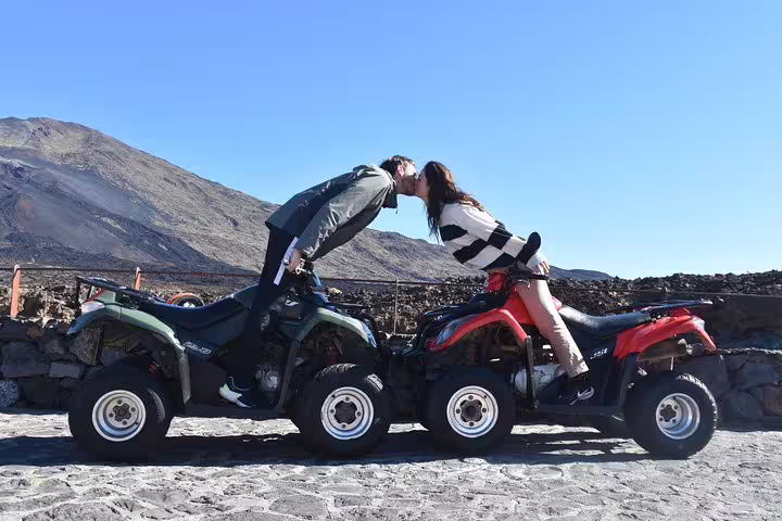 Couple sharing a kiss on quad bikes at Teide Volcano National Park, with a scenic mountain view.