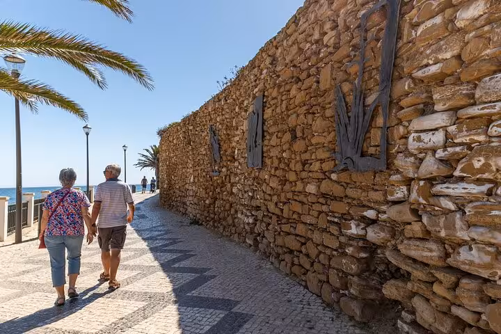 Couple walking along a scenic Lagos promenade with ocean views and stone walls during a private city tour.