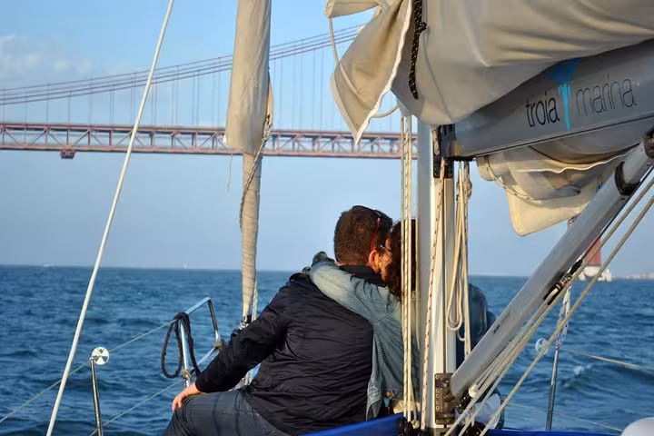 Couple cuddling on private Lisbon sunset sailboat cruise on the Tagus River near 25 de Abril Bridge