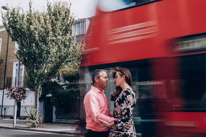 Couple embraces on a London street as a red double-decker bus speeds by, capturing the city's vibrant energy.