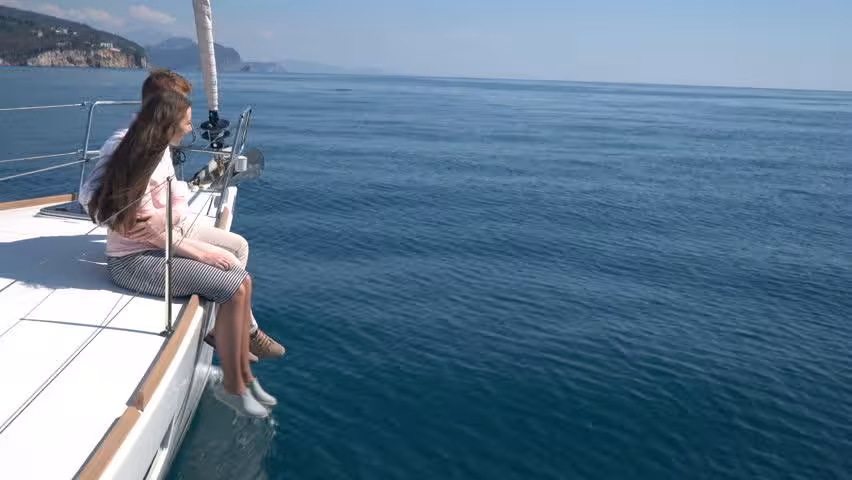 Couple sitting on the bow of a luxury sailboat on calm blue water, Lisbon romantic sailing tour