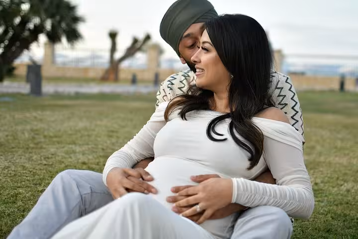 Happy couple embracing tenderly on grass, capturing a beautiful maternity moment in Ammoudara's scenic setting.