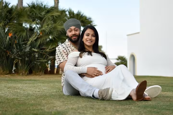 Smiling couple seated on grass in Ammoudara, embracing maternity bliss during a private photoshoot session.