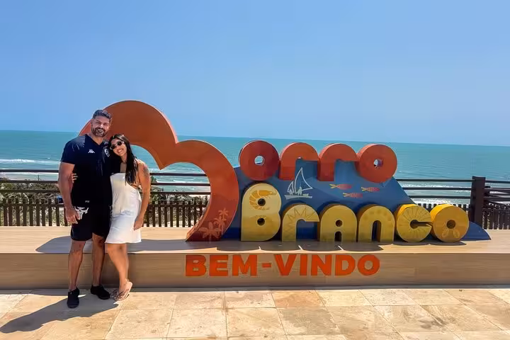 Couple at Morro Branco welcome sign by the ocean, starting a 3 beaches in 1 day Ceará tour