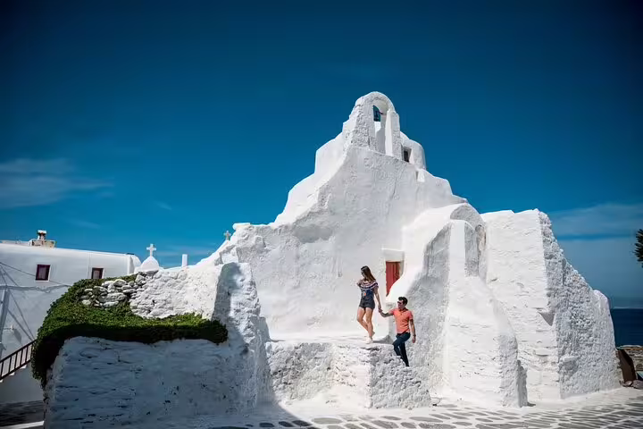 Couple posing on steps of a whitewashed Mykonos chapel, private photoshoot with professional photographer in Greece