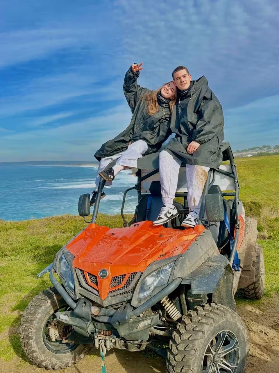 Couple posing on orange off-road buggy by ocean cliffs during Blazing Trails Buggy Tour coastal adventure