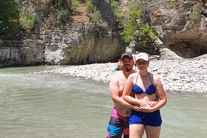 Couple enjoying a sunny day by the river in Osum Canyon, Albania, with rocky cliffs and clear waters.