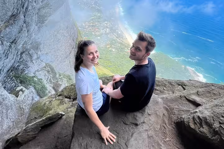 Couple sitting on Pedra da Gávea's rock, overlooking breathtaking ocean and forest views on Garganta do Céu hike.