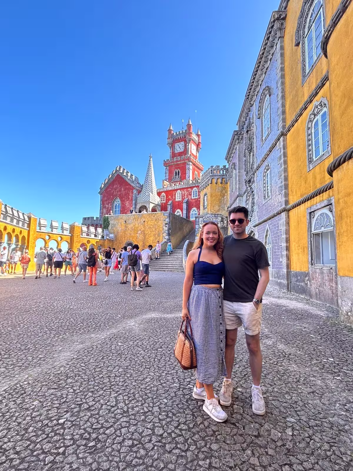 Couple poses in front of Sintra's colorful Pena Palace, highlighting its unique design and historic charm.