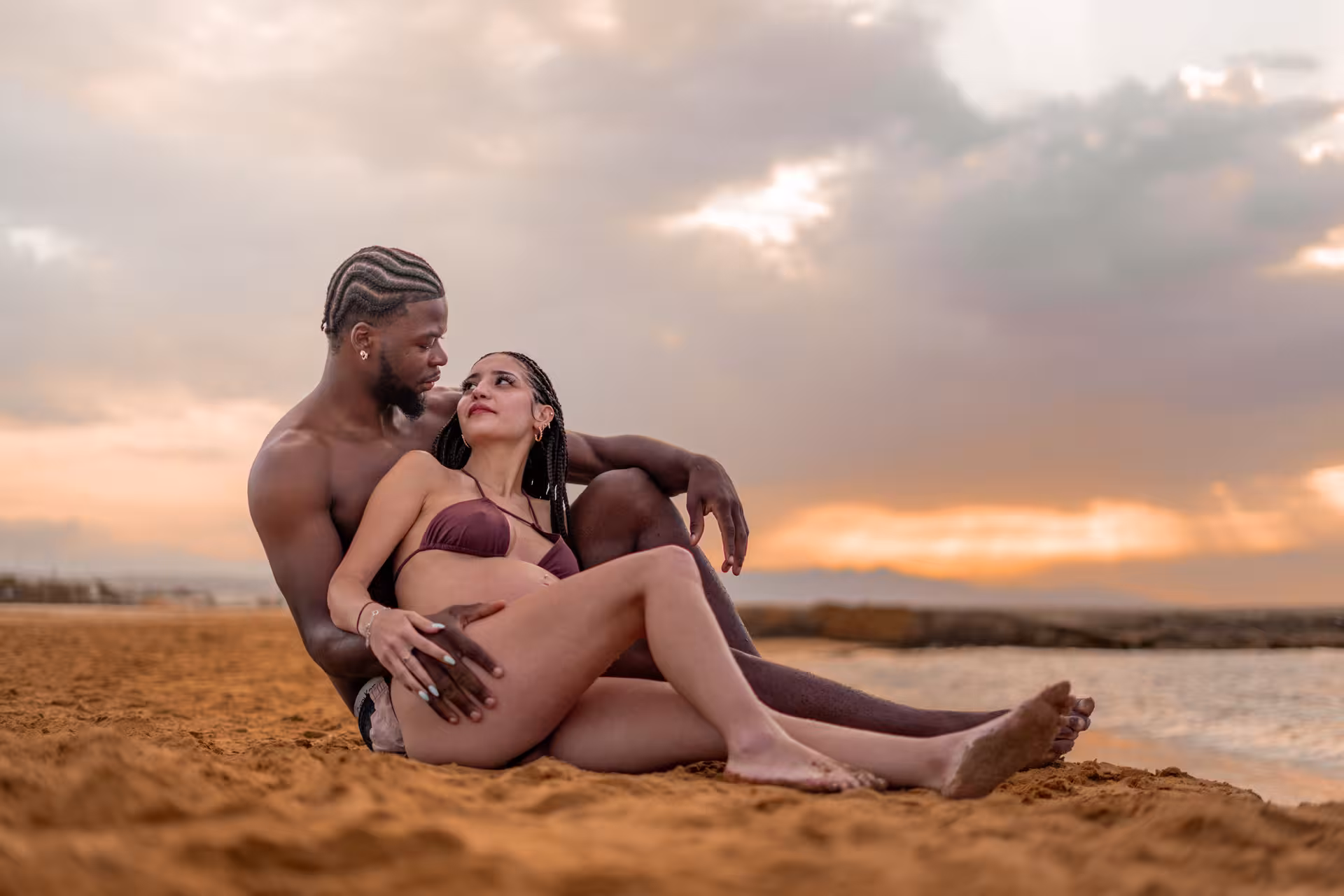 Romantic couple seated on a sandy beach at Heraklion during sunset, highlighting a serene photoshoot setting.