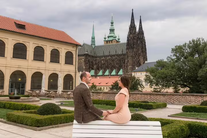 Couple sits on a bench in a garden with a view of St. Vitus Cathedral, enjoying a serene moment in Prague.