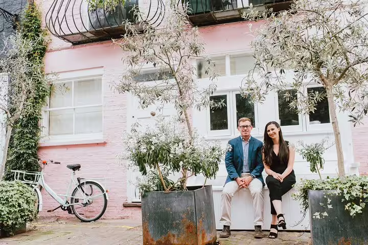 Couple poses in front of charming pink house with bicycle during private travel photographer tour in London.