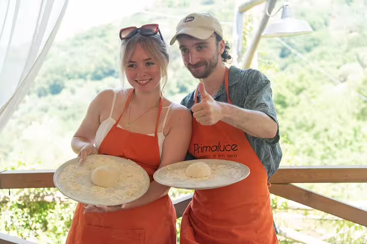 Couple in aprons holds fresh pizza dough during farm pizza-making class with wine and limoncello tasting