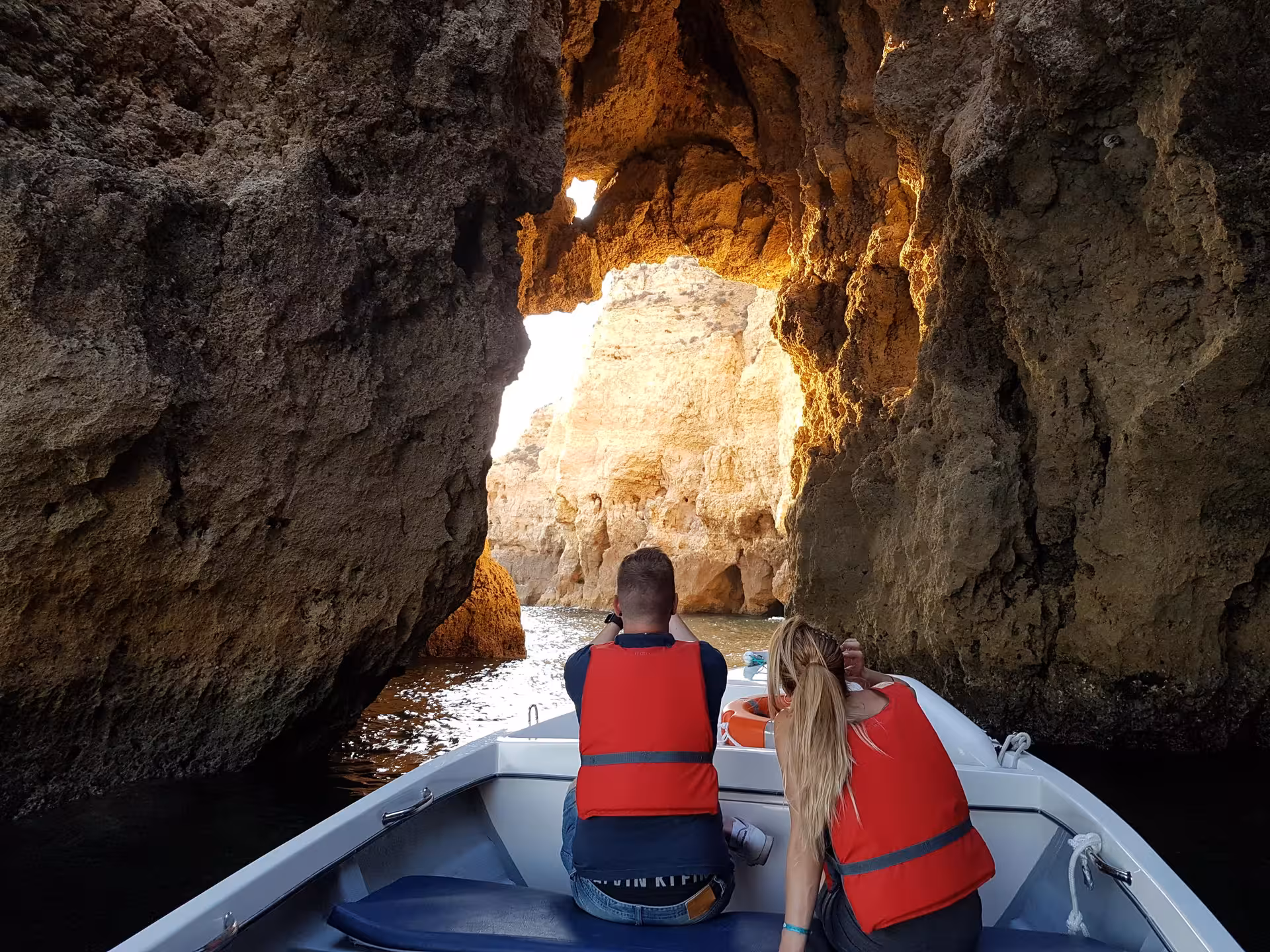 Couple in life jackets on a Ponta da Piedade grotto boat tour, cruising beneath dramatic golden rock arches near Lagos