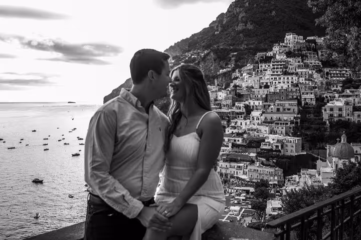 Couple sitting and smiling with a stunning view of Positano's hillside architecture and the sea on an Amalfi Coast tour.