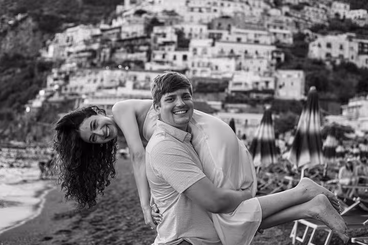 Couple enjoying a playful moment on Positano beach with scenic Amalfi Coast backdrop, perfect for romantic photo shoots.