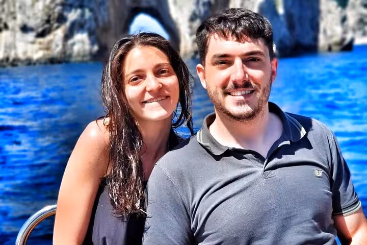 Couple enjoying a sunny day on a private boat tour near Capri's iconic rock formations with crystal blue waters.